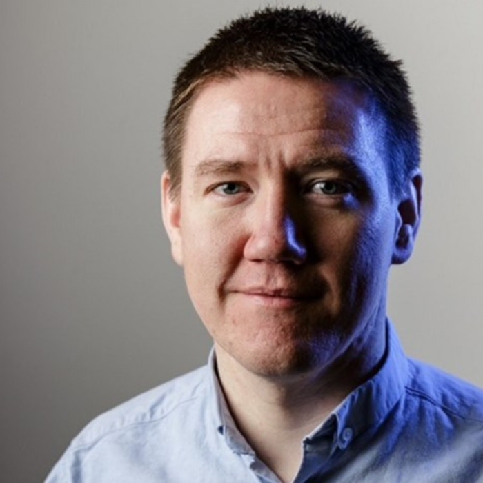 Um homem de cabelo curto e escuro, vestido com uma camisa de botões azul clara, aparece pronto para treinar. O pano de fundo passa graciosamente de cinzento para azul.