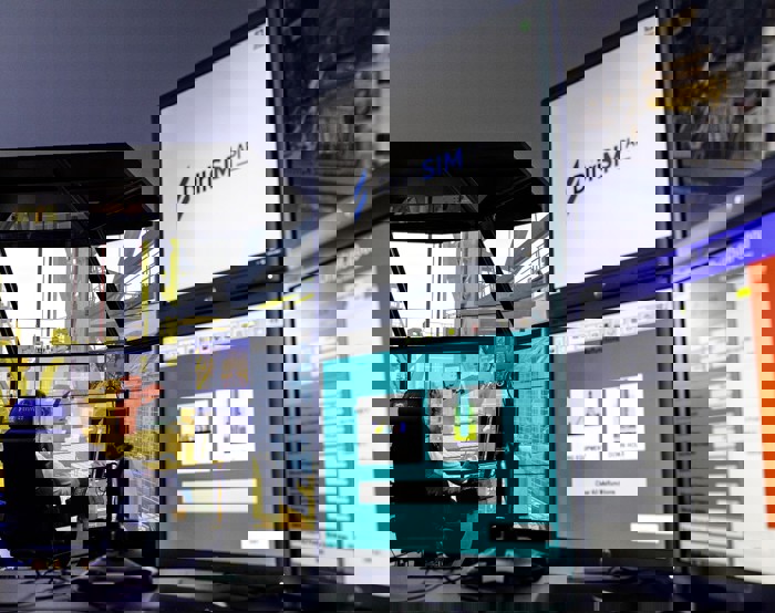 Múltiplos monitores de computador numa sala de controlo apresentam software de simulação para operações de perfuração, com um ecrã a mostrar "DrillSIM API". Uma pessoa está sentada, concentrada no grande monitor central.