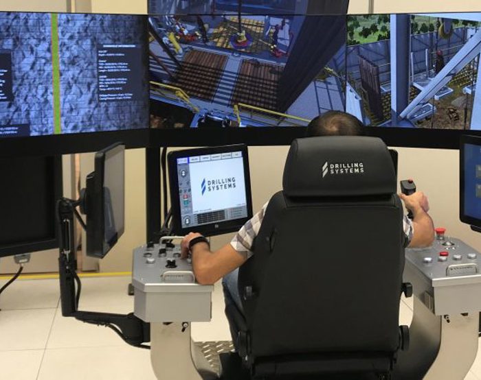 Pessoa que opera um simulador de perfuração com vários ecrãs e painéis de controlo.