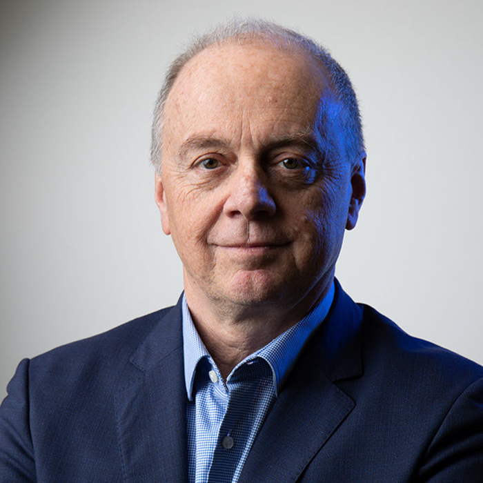 رجل في منتصف العمر مع انحسار خط الشعر، يرتدي سترة بدلة زرقاء وقميصاً أزرق، ويقف على خلفية بسيطة مع تعبيرات محايدة.