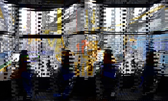 Duas pessoas sentam-se em postos de controlo com vários monitores, operando um simulador de perfuração de alta tecnologia. Grandes ecrãs simulam um ambiente de perfuração offshore à sua volta.