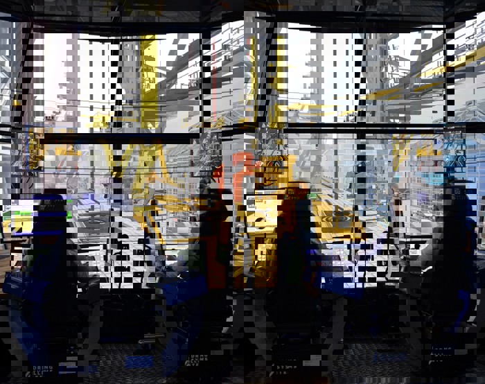 Duas pessoas sentam-se em postos de controlo com vários monitores, operando um simulador de perfuração de alta tecnologia. Grandes ecrãs simulam um ambiente de perfuração offshore à sua volta.