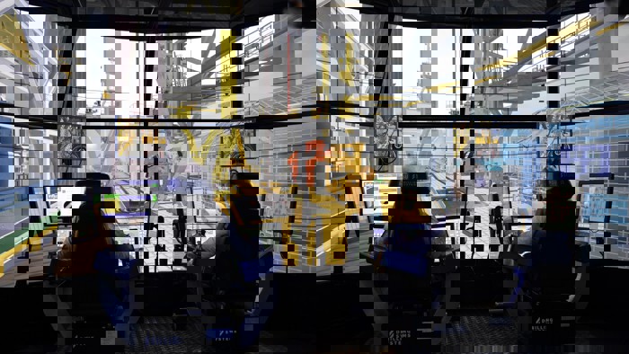 Duas pessoas sentam-se em postos de controlo com vários monitores, operando um simulador de perfuração de alta tecnologia. Grandes ecrãs simulam um ambiente de perfuração offshore à sua volta.