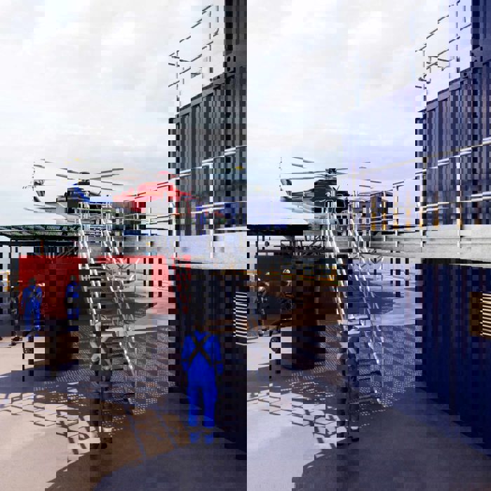 Helicóptero sobre una plataforma con trabajadores de uniforme azul cerca, situado junto a contenedores metálicos.