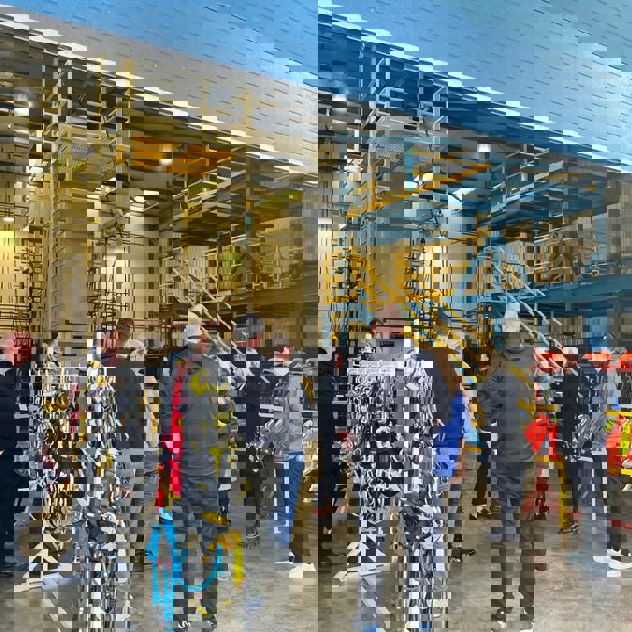 A group of people gathered in a warehouse with safety equipment and harnesses on display racks.