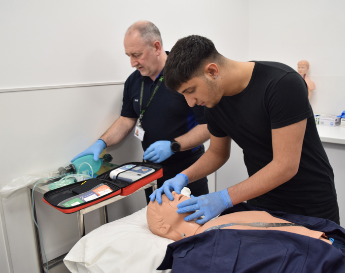 يتدرب شخصان على الإنعاش القلبي الرئوي على عارضة أزياء طبية. يقوم أحدهما بمراقبة المعدات، بينما يقوم الآخر بالضغط على الصدر. ويرتدي كلاهما قفازات.