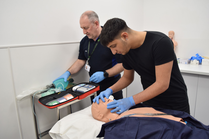 يتدرب شخصان على الإنعاش القلبي الرئوي على عارضة أزياء طبية. يقوم أحدهما بمراقبة المعدات، بينما يقوم الآخر بالضغط على الصدر. ويرتدي كلاهما قفازات.