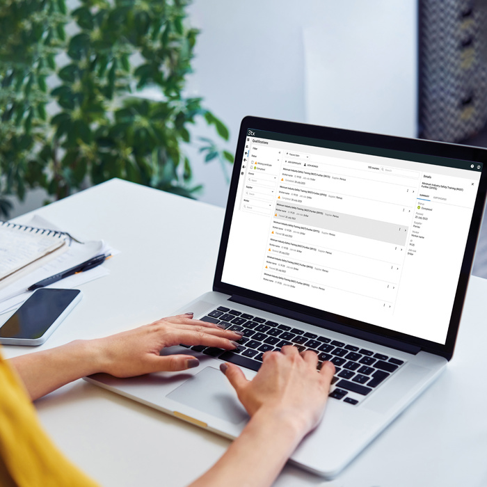 شخص يكتب على جهاز كمبيوتر محمول على مكتب مع صندوق بريد إلكتروني مفتوح على الشاشة، وبجانبه دفتر ملاحظات وقلم وهاتف ذكي وكوب من الماء. توجد نبتة في الخلفية.