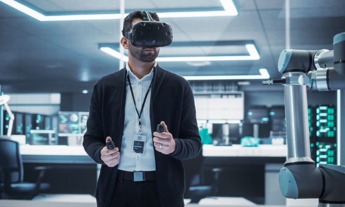 Una persona con un casco de realidad virtual maneja un brazo robótico con unos mandos manuales en una moderna sala de alta tecnología.