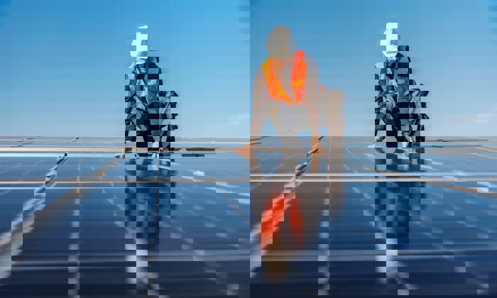 Trabalhador com colete e capacete de segurança instala painéis solares num dia de sol.