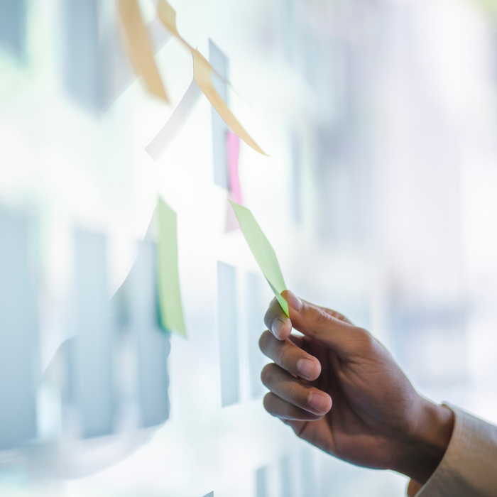 يد تقوم بترتيب الملاحظات اللاصقة الملونة بشكل منهجي على سطح زجاجي، كما لو كانت تهيئ المسرح لجلسة تدريب إبداعية.