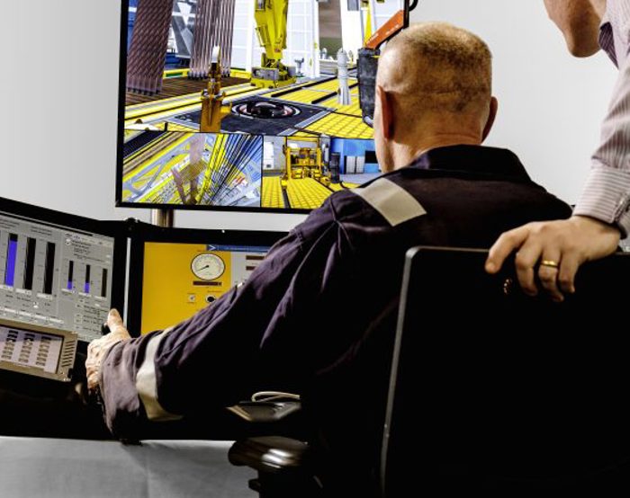 Dois indivíduos numa sala de controlo, onde um deles opera vários monitores que apresentam vários dados e um cenário de construção.