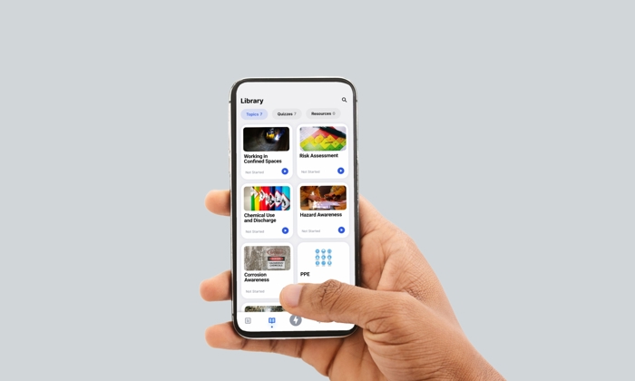 Uma mão segura um smartphone que apresenta uma biblioteca de cursos relacionados com segurança, incluindo Trabalho em espaços confinados, Avaliação básica e EPI, entre outros.