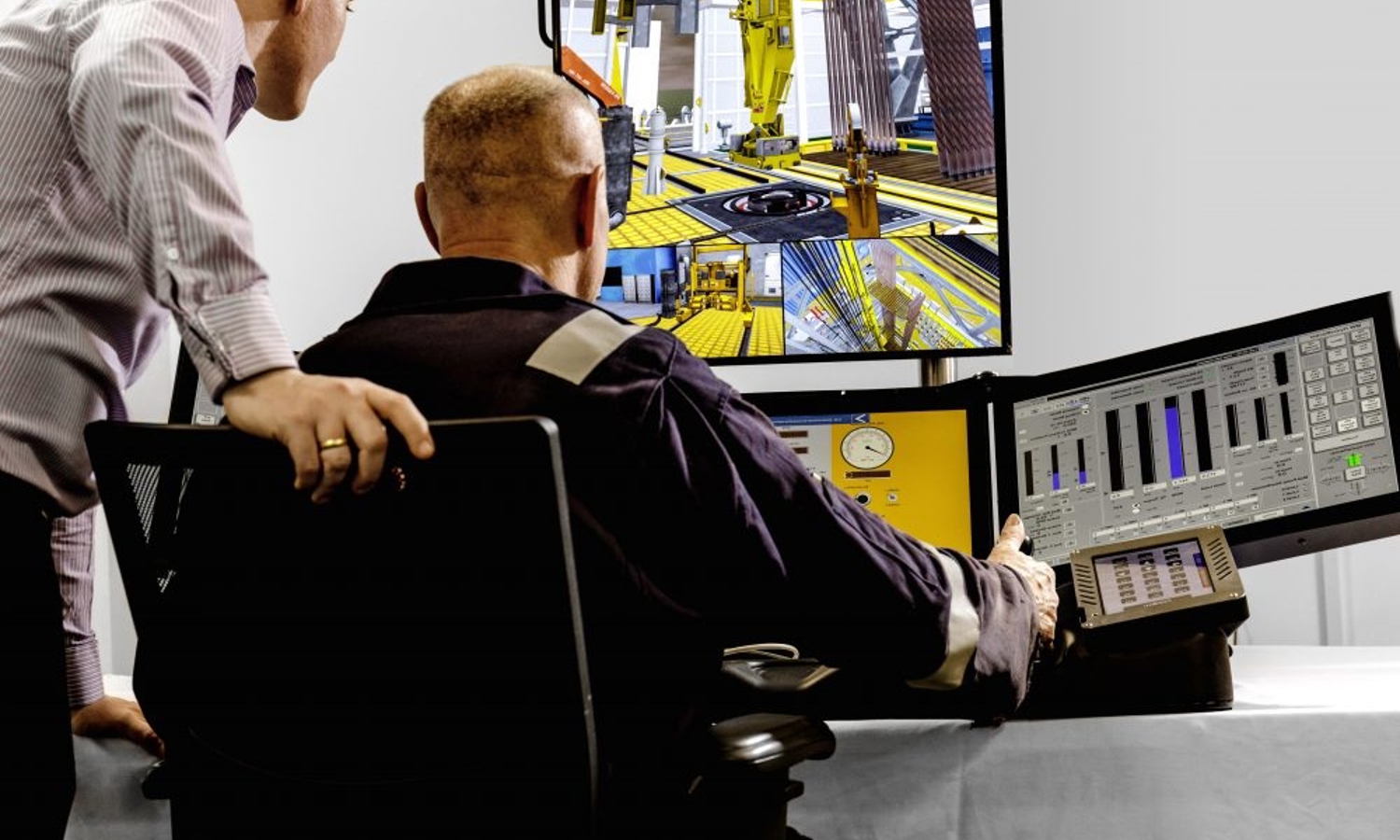 Dois homens numa sala de controlo monitorizam vários ecrãs que apresentam maquinaria industrial e gráficos de dados. Um homem está sentado enquanto o outro se inclina para observar os ecrãs.