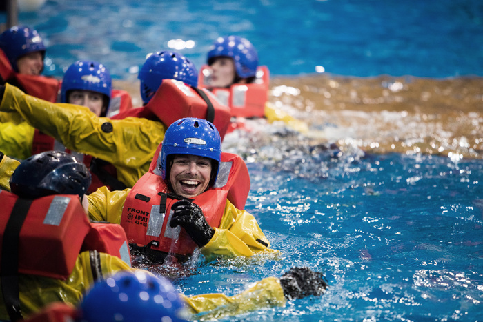 Personas con chalecos salvavidas y cascos participan en una formación sobre seguridad en el agua, sonriendo e interactuando en una piscina.