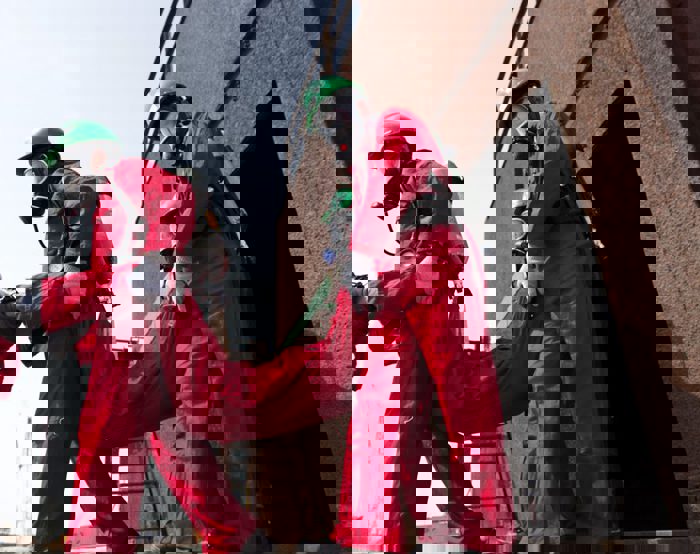 مستجيبو الطوارئ الذين يرتدون بدلات واقية حمراء وخوذات خضراء يحملون شخصًا إلى أعلى سلم معدني.