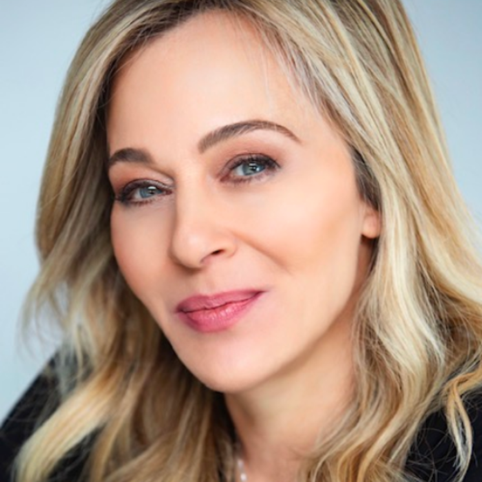 امرأة ذات شعر أشقر طويل وعينين زرقاوين، تبتسم بهدوء، وترتدي قميصاً أسود.